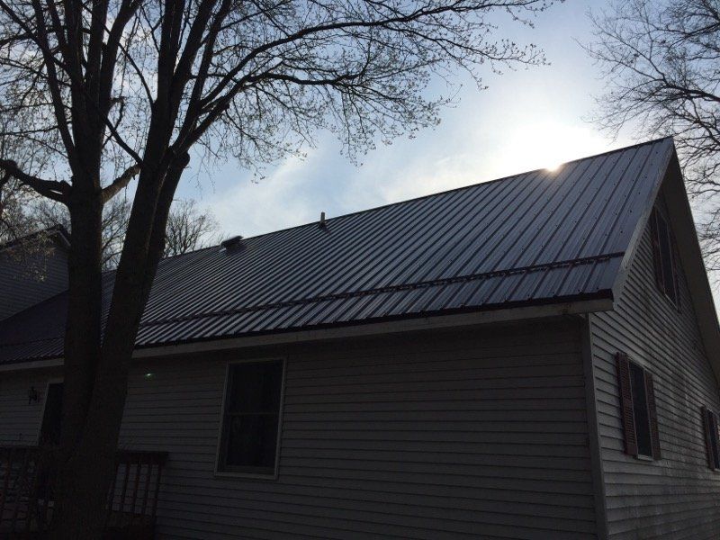 Gray house with metal roof, sun shining through the trees.