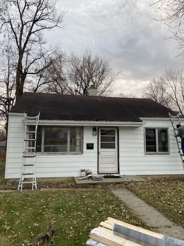 White house under cloudy sky. Two ladders lean against the roof. One person on a ladder.