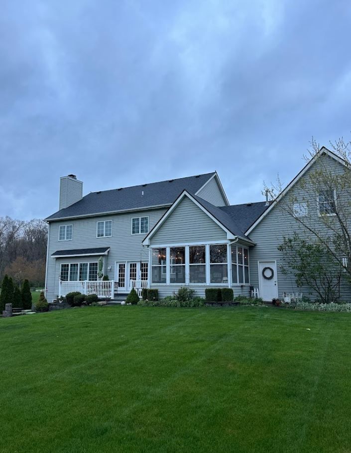 Two-story gray house with a screened-in porch, on a green lawn under a cloudy sky.