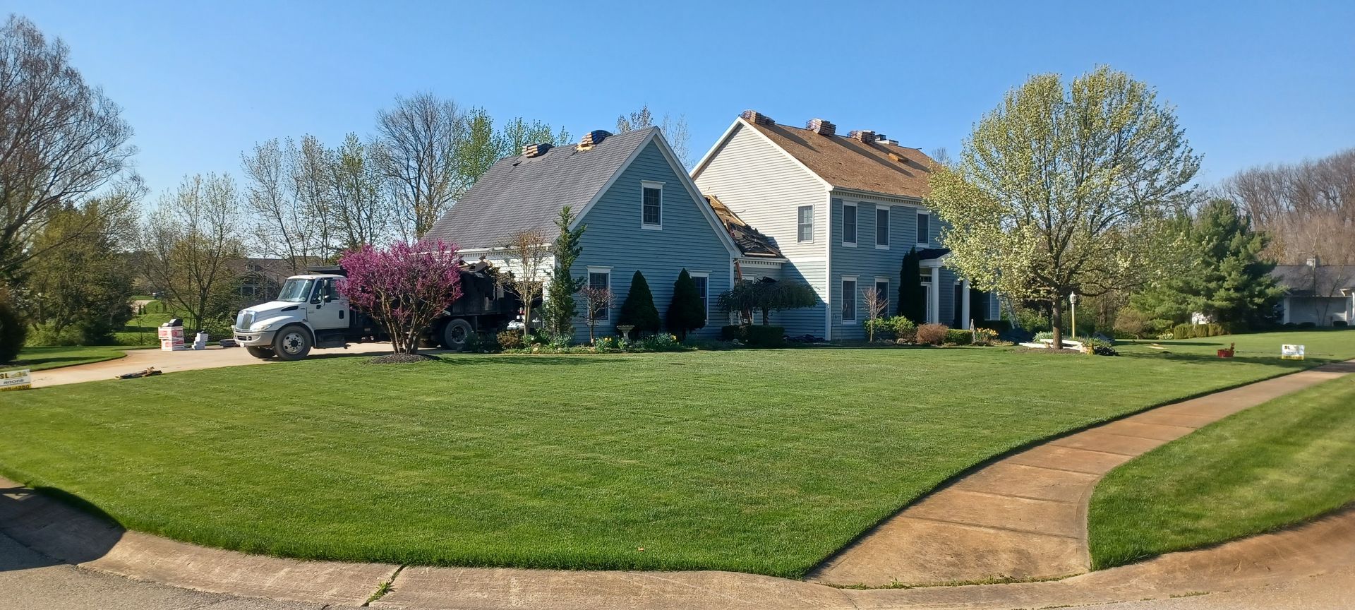A well-manicured green lawn leads to a two-story blue house on a sunny day. A white truck is parked.