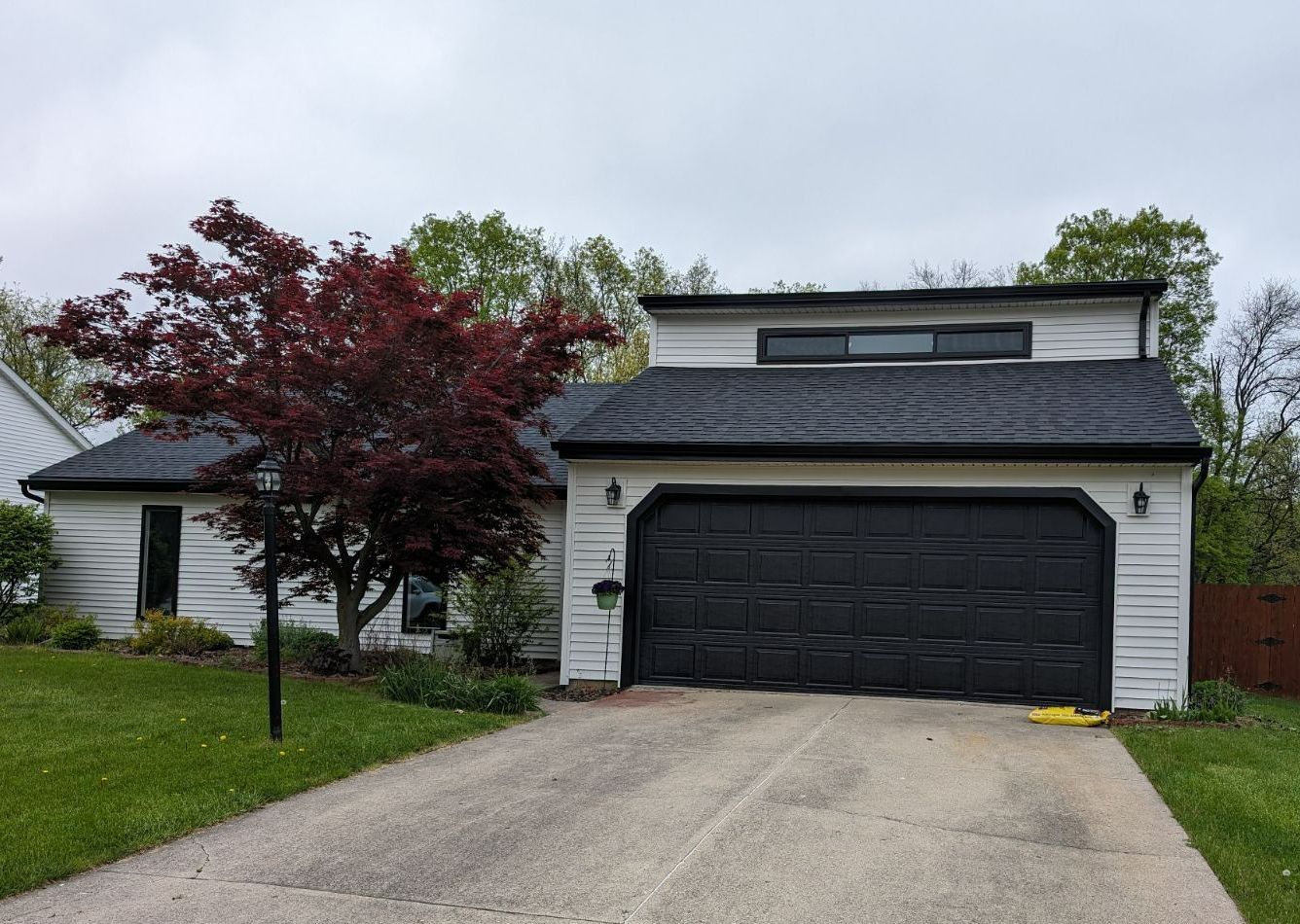 White house with black garage door and a red tree in front.
