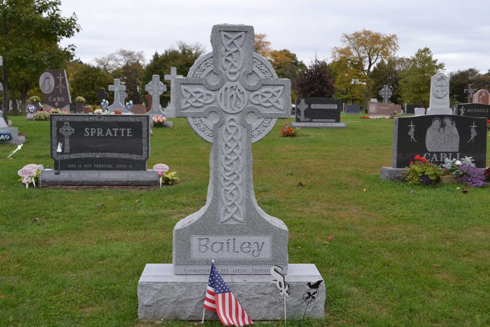 Celtic cross headstone in a cemetery with an American flag.