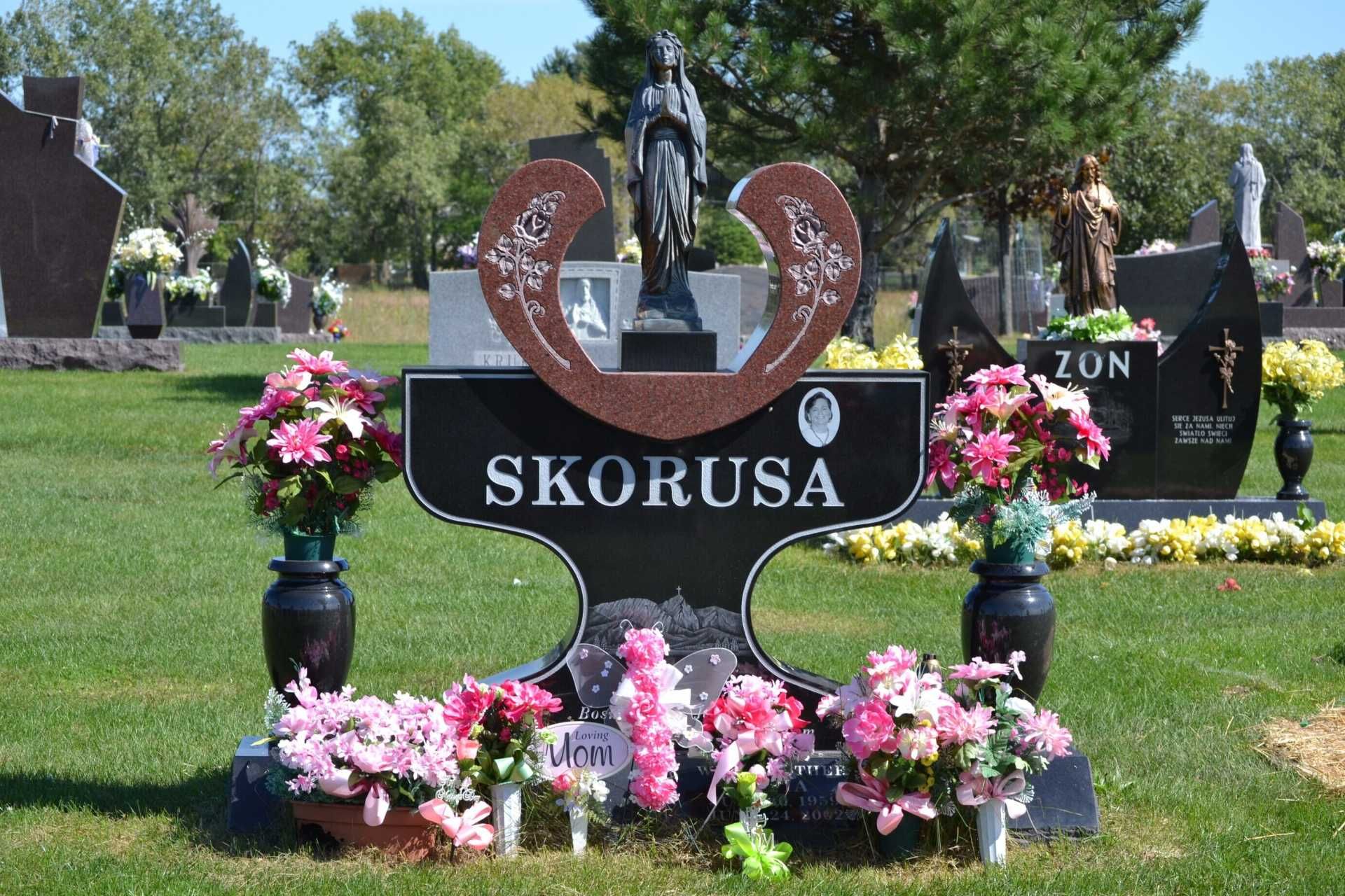 Gravestone with floral arrangements; a statue sits on top.