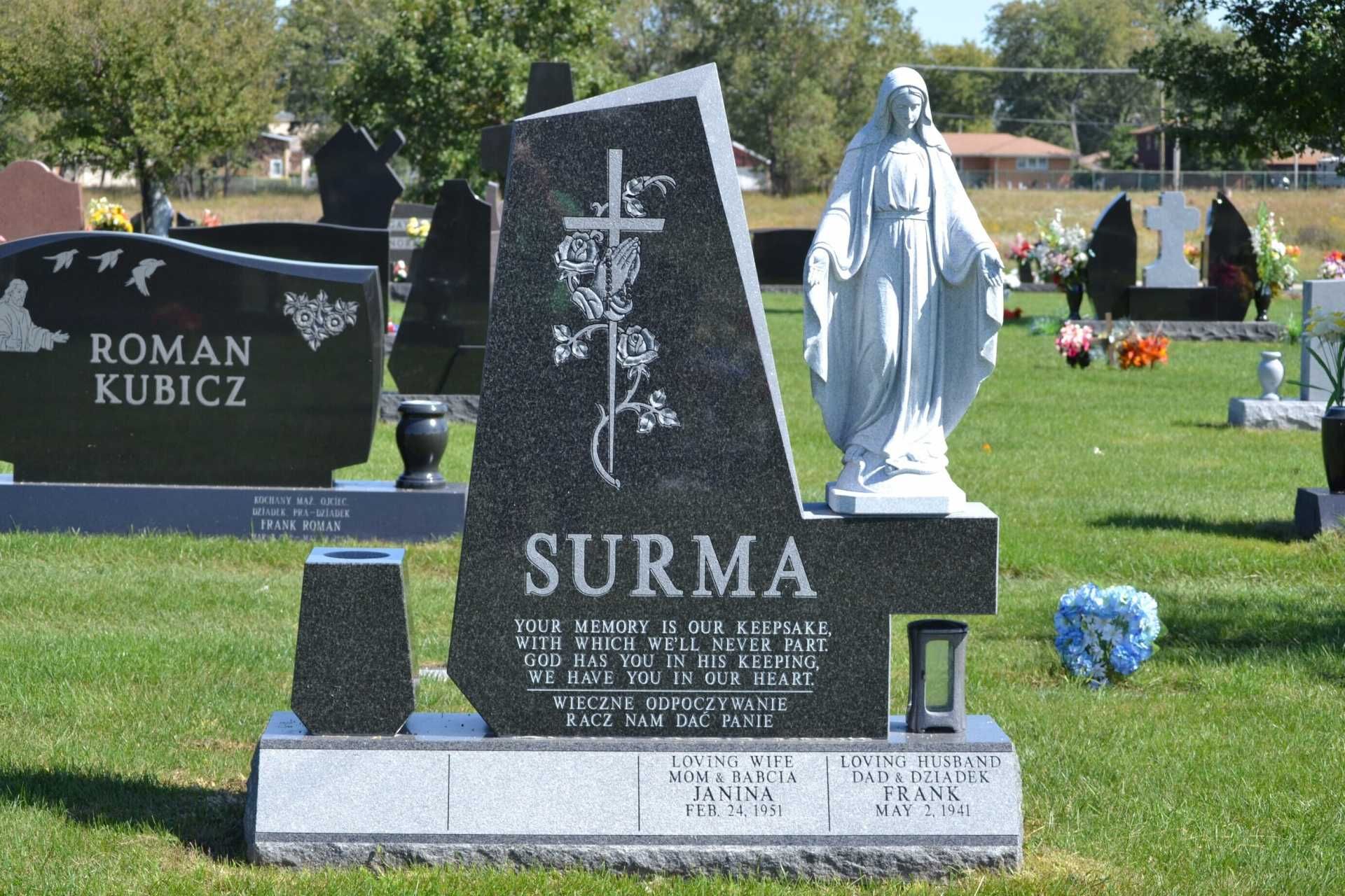 Headstone in a cemetery with a statue of the Virgin Mary, cross, and the name