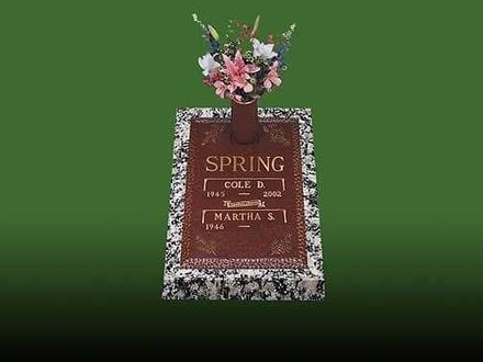 Tombstone with flowers. Red-brown surface with names "Cole" and "Martha" on a marble base against a green background.
