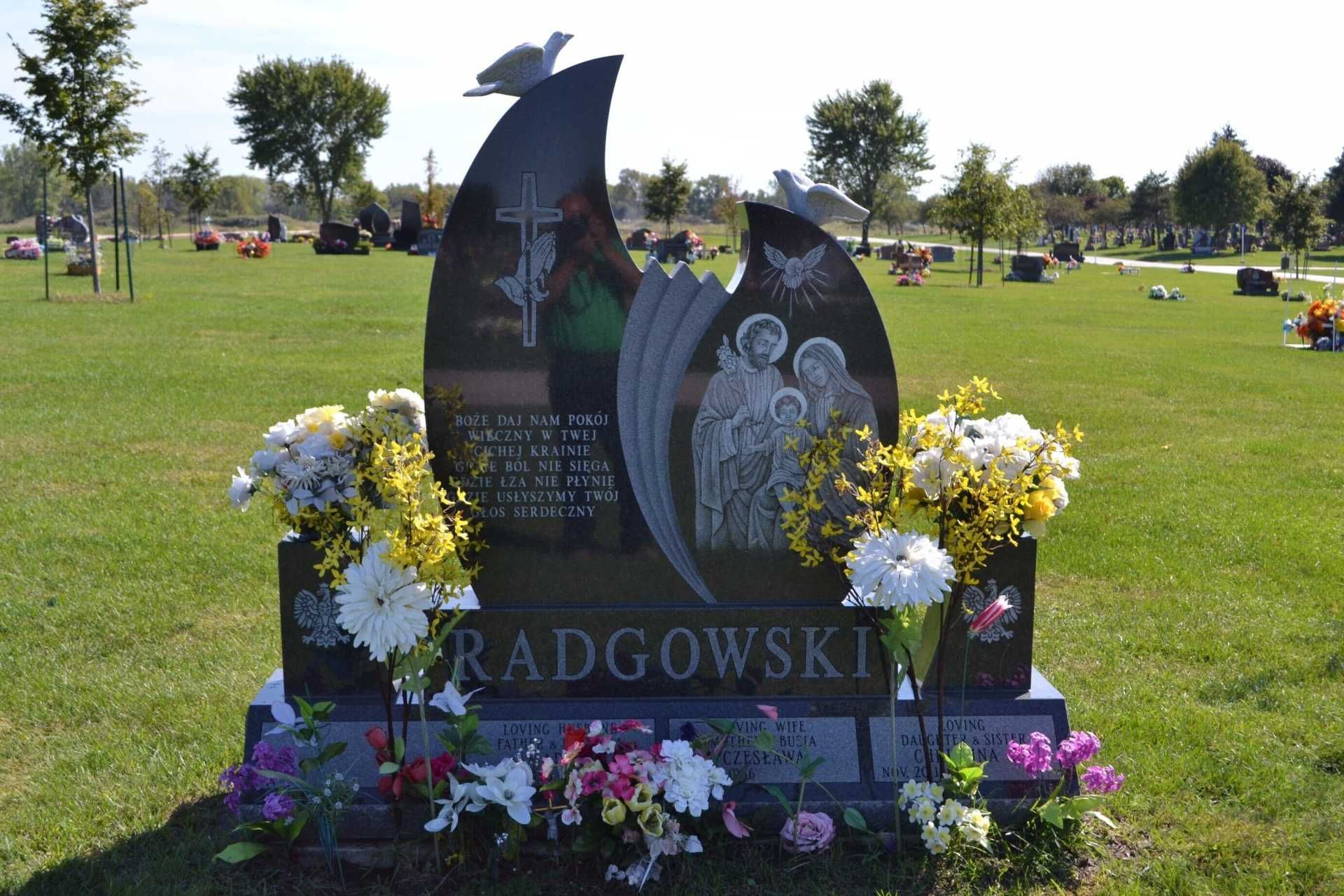 Headstone in a cemetery with flowers. The stone has an angel carving and two doves on top.