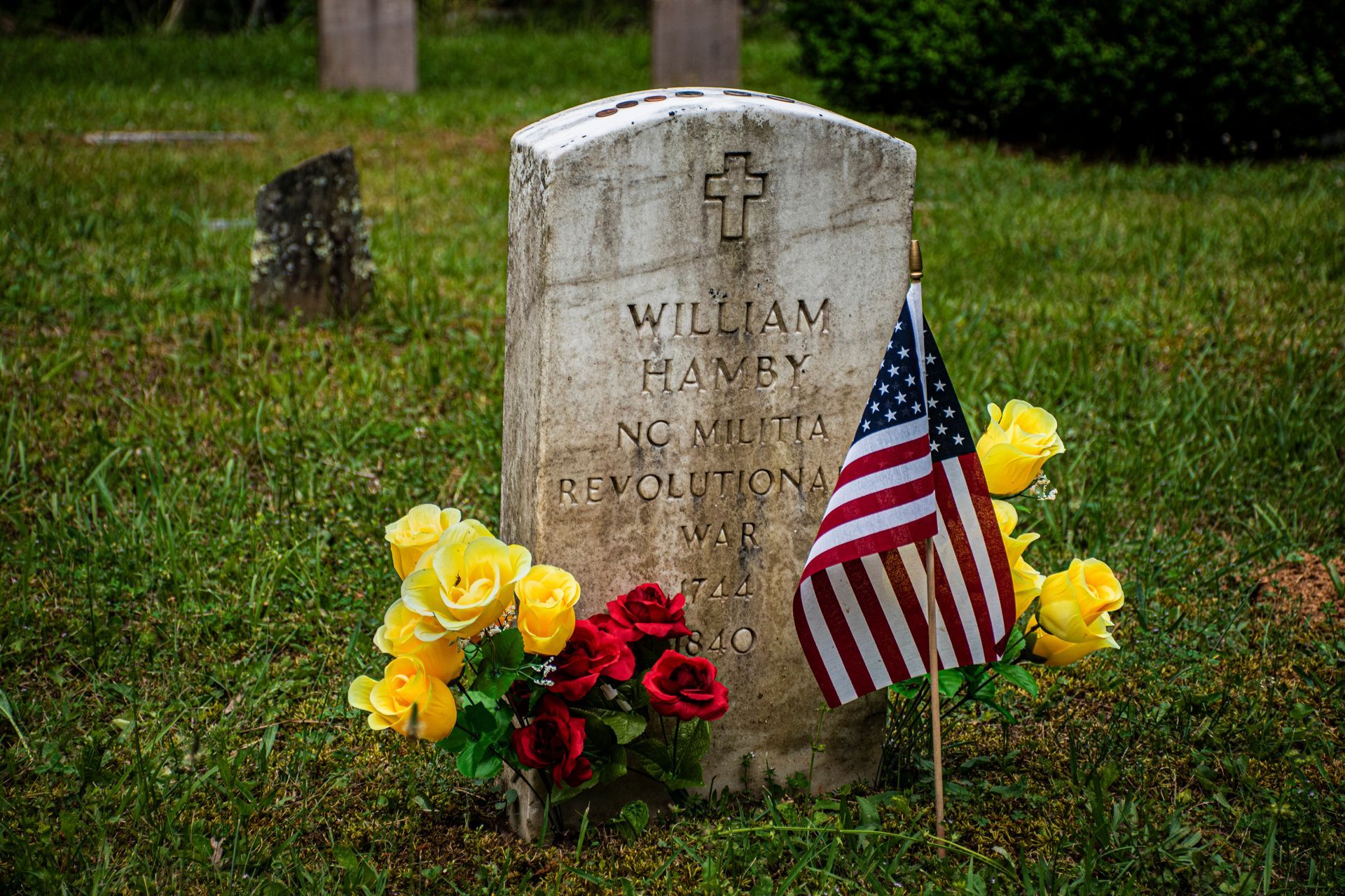 Grave marker with flowers and a flag honoring a revolution-era soldier