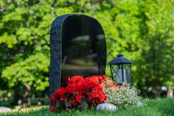 Black tombstone with red flowers and a lantern in a green, outdoor setting.