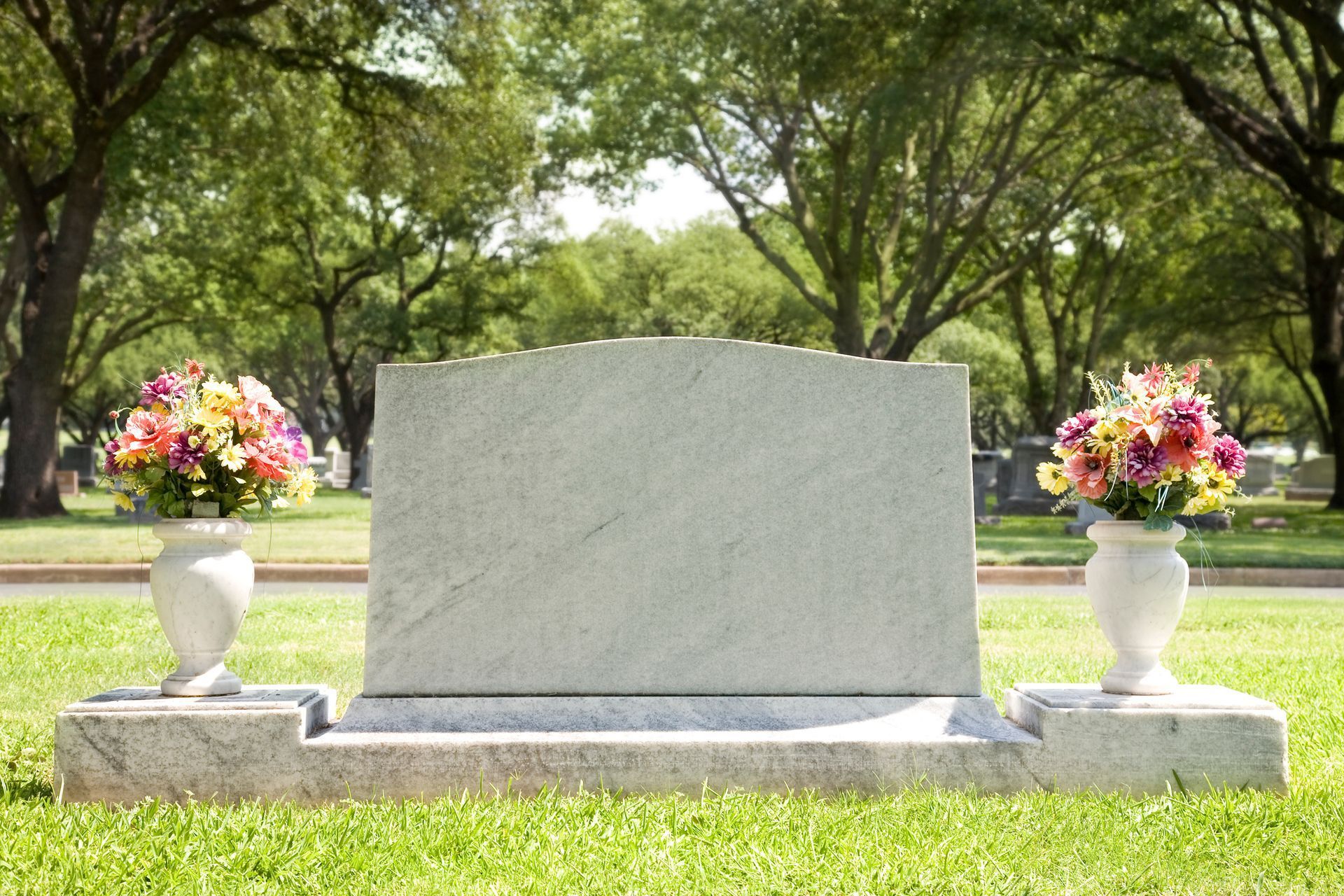 Blank tombstone with floral arrangements, outdoors in a green grassy cemetery.