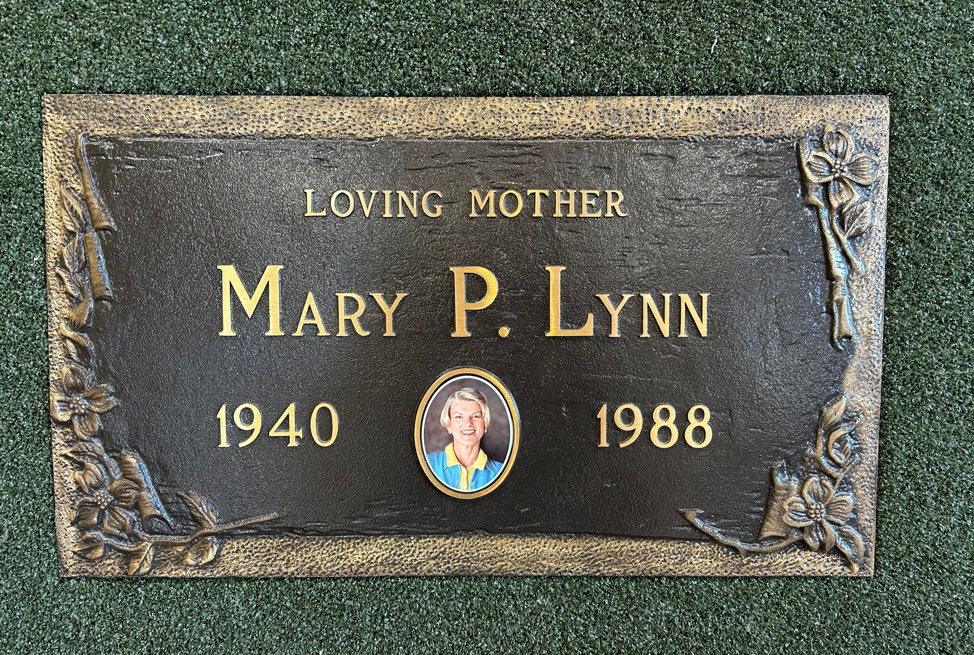 Bronze memorial plaque with flowers, green surface, and name 