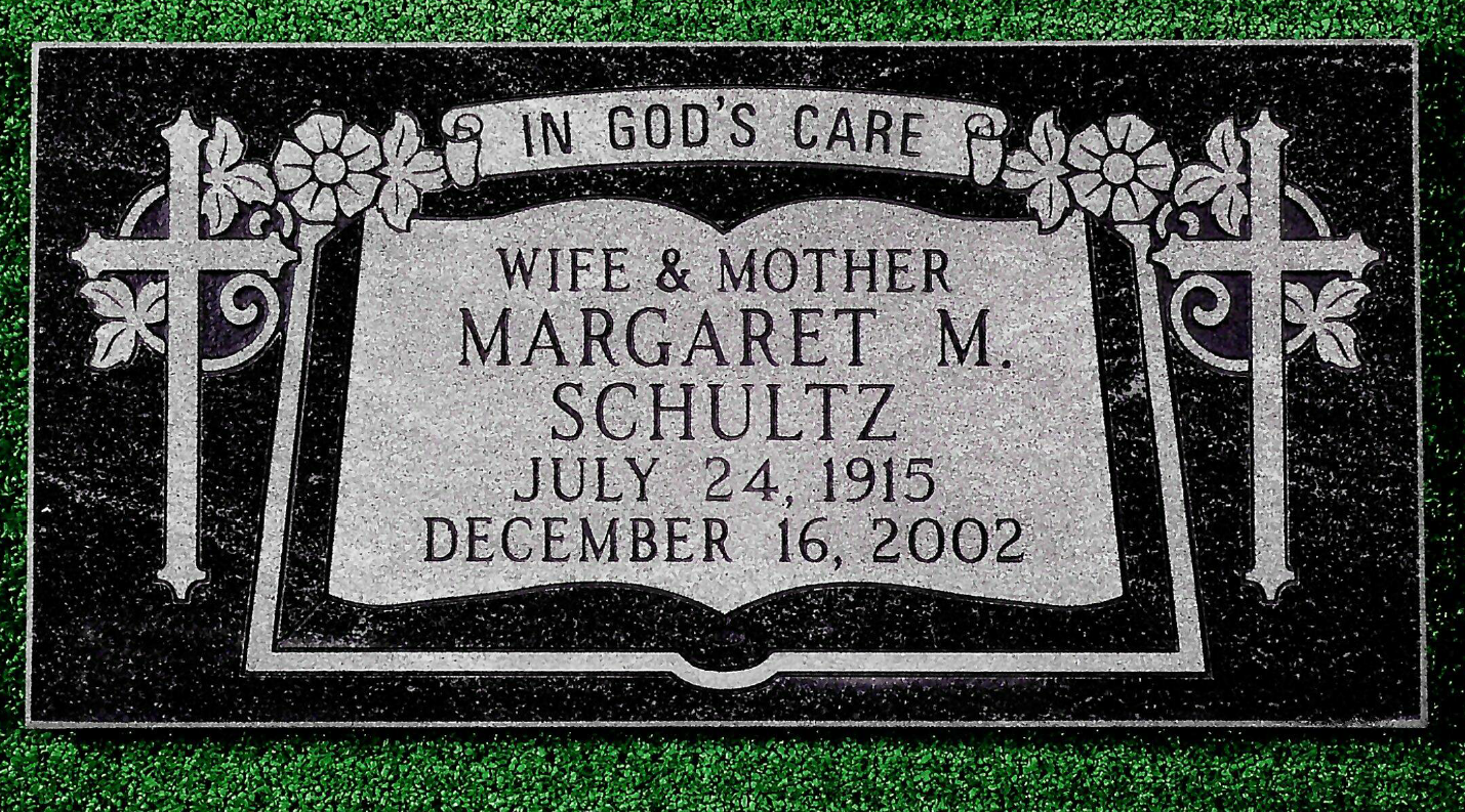 A black granite memorial plaque for Margaret M. Schultz, featuring an open book design, engraved crosses, and flowers.