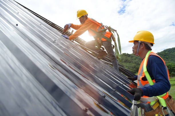 Two local roofers in orange safety vests and helmets repairing a roof.