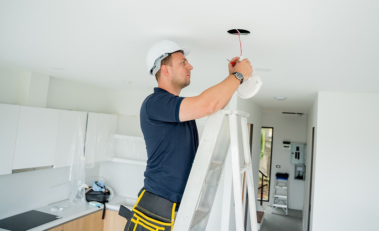 A Man is Standing on a Ladder Fixing a Light Fixture on the Ceiling — Brite-Lec Pty Ltd in Currajong, QLD