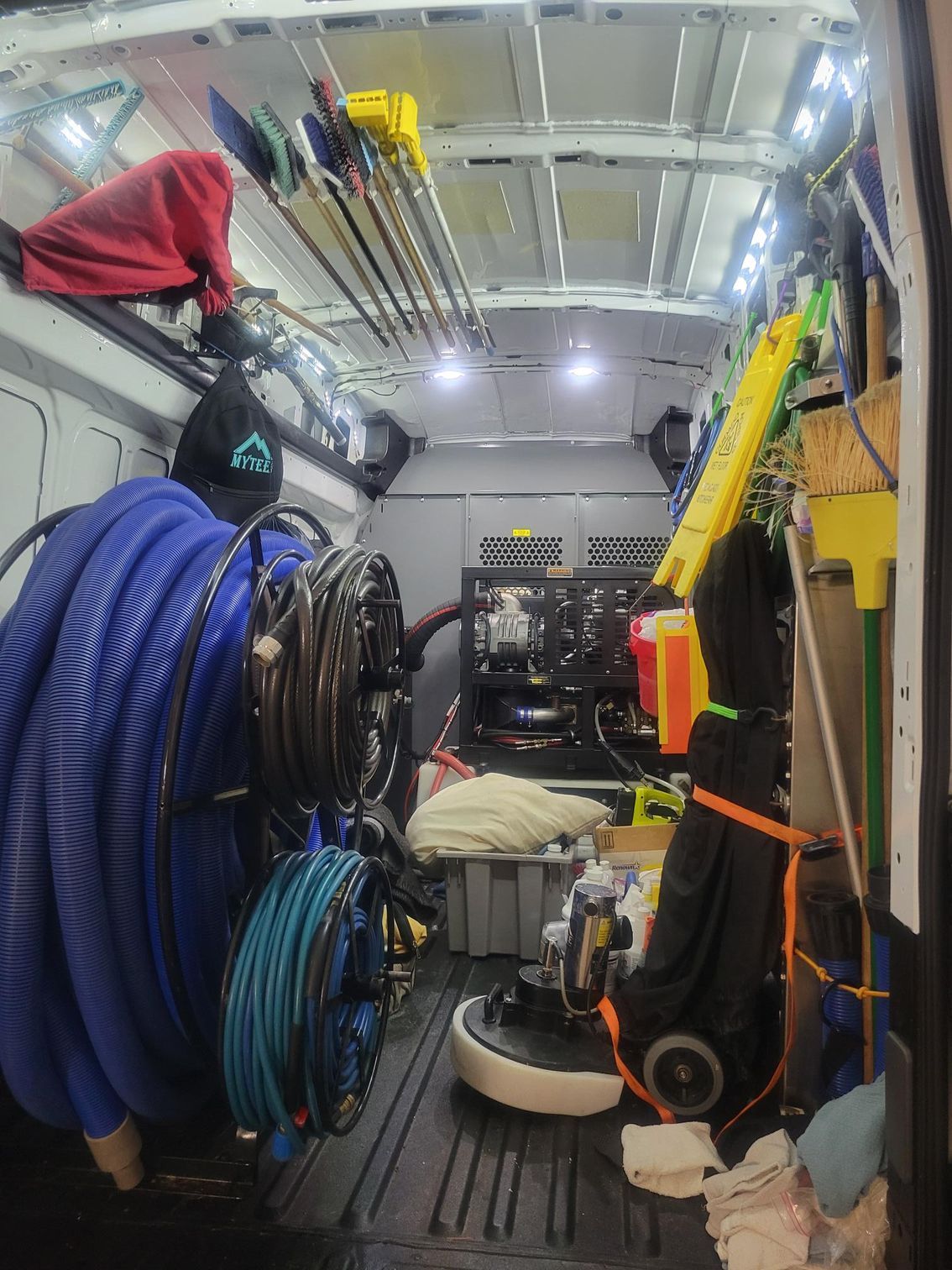 A mop , bucket , spray bottles and brushes are on the floor in a living room.