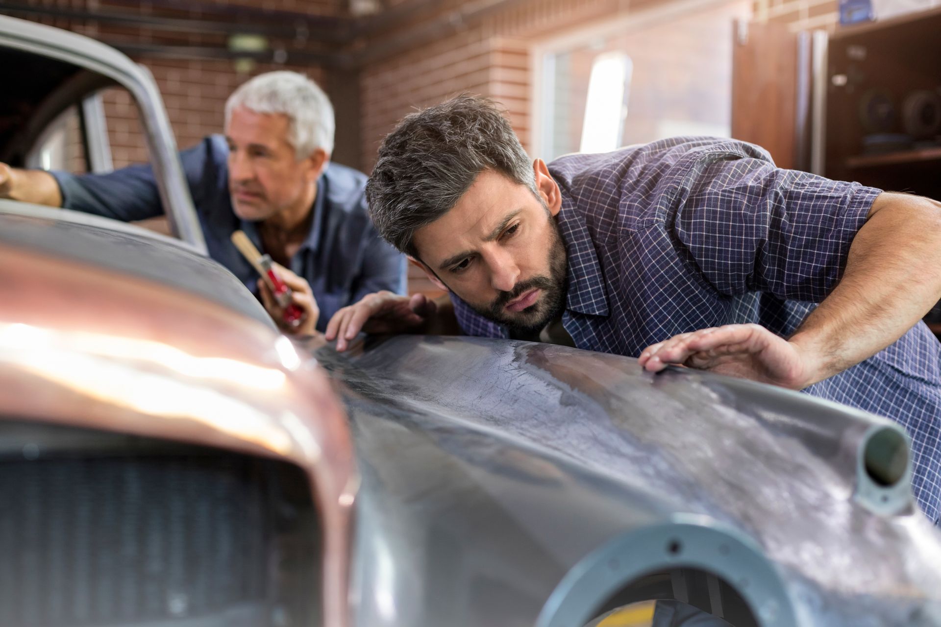 Two focused mechanics examining a classic car panel in an auto repair shop.