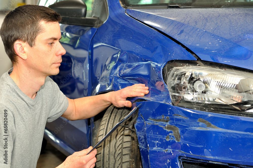 A mechanic holds a tablet while inspecting the damage of a car in an auto repair garage. A mechanic holds a tablet while inspecting the damage of a car in an auto repair garage.