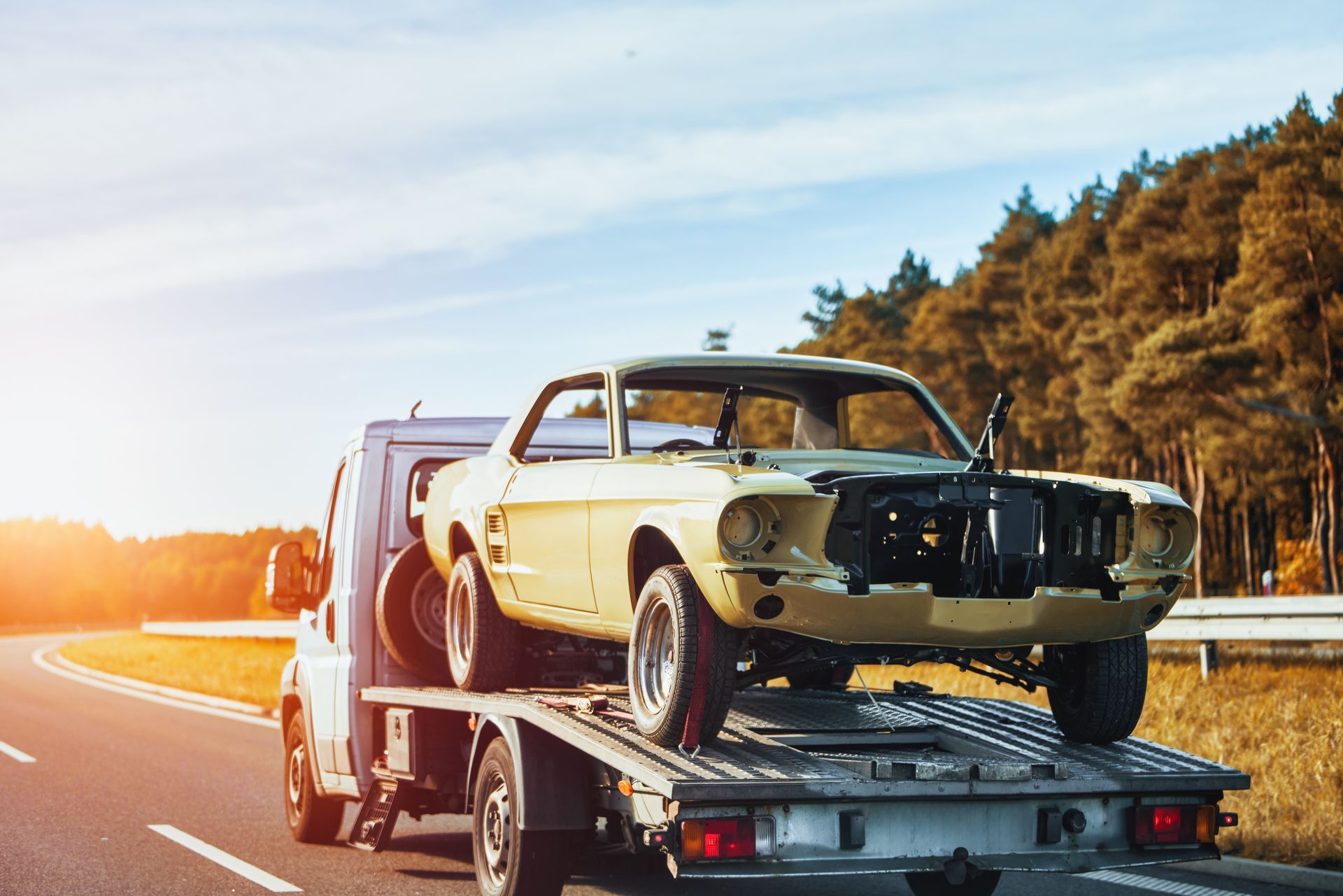 A tow truck in motion on a road with a damaged classic vehicle after being in a traffic accident. A tow truck in motion on a road with a damaged classic vehicle after being in a traffic accident.