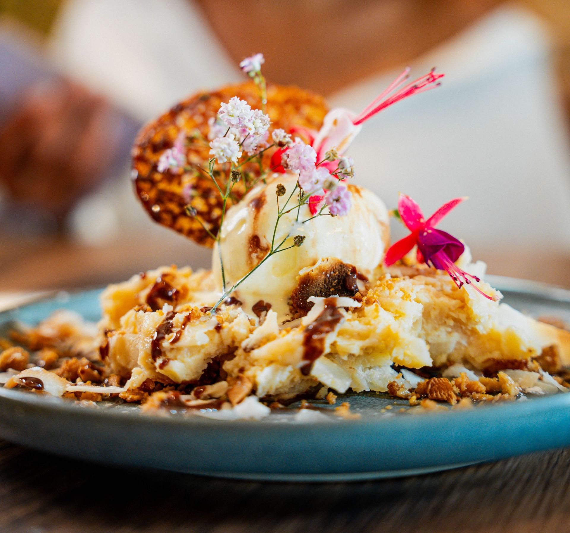Sobremesa com sorvete, chocolate granulado e flores em um prato azul.
