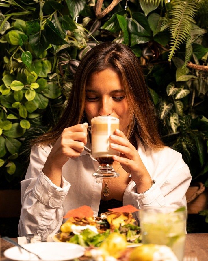 Uma mulher está sentada à mesa tomando uma xícara de café.
