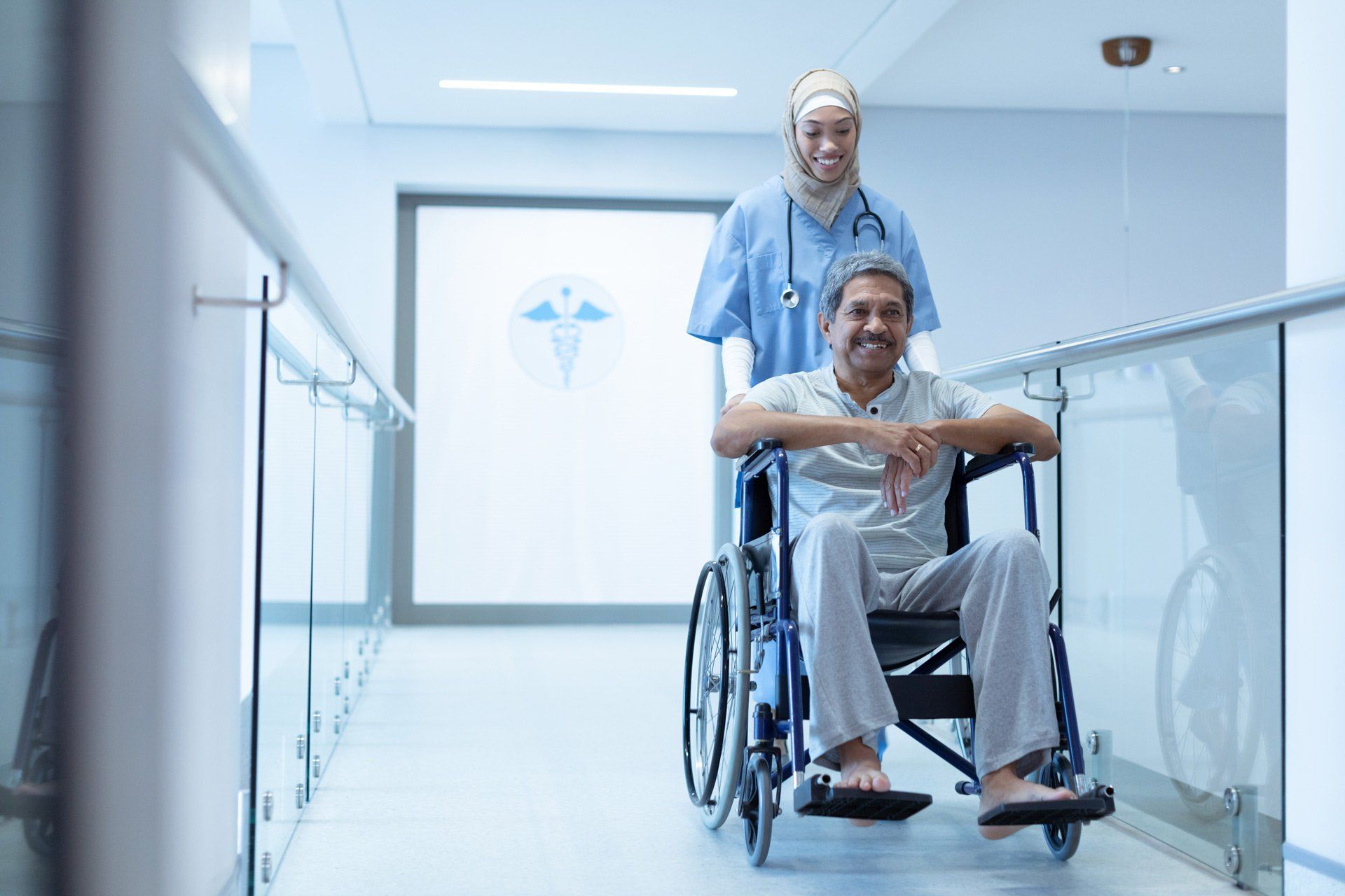 side-view-of-mixed-race-female-doctor-in-hijab-pushing-senior-mixed-race-male-patient-in-wheelchair-1435068716