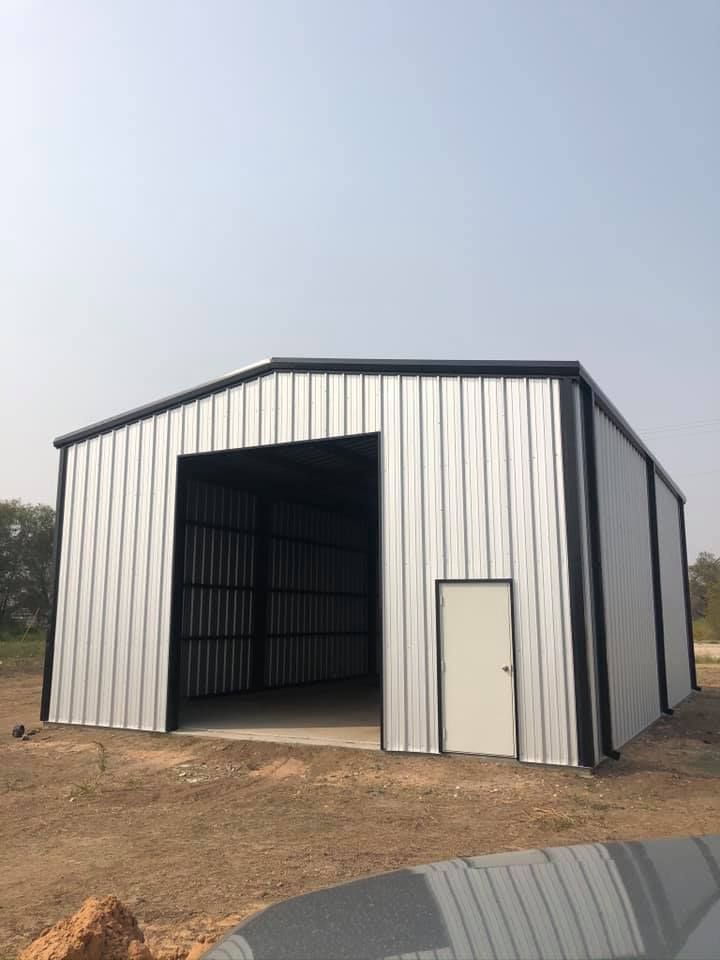 A large metal building with a large door is sitting in the middle of a dirt field.