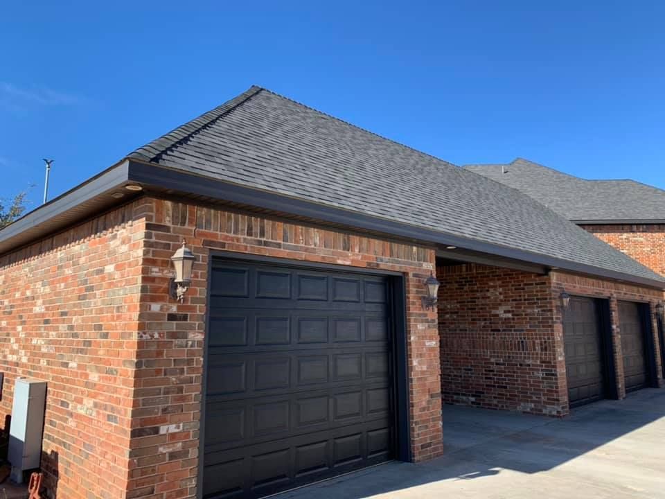 A brick garage with two black garage doors and a gray roof.