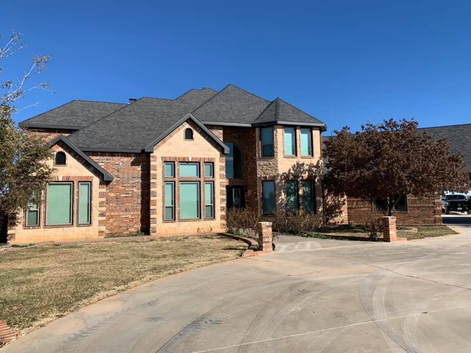 A large brick house with a gray roof is sitting on top of a lush green field.
