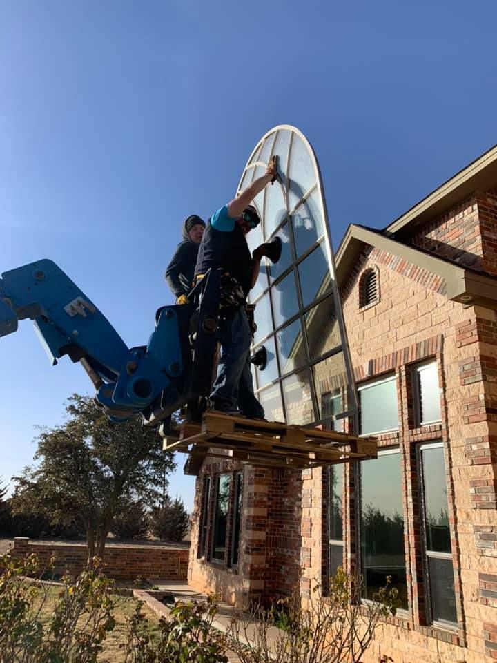 Two men are installing a large glass window on the side of a brick house.