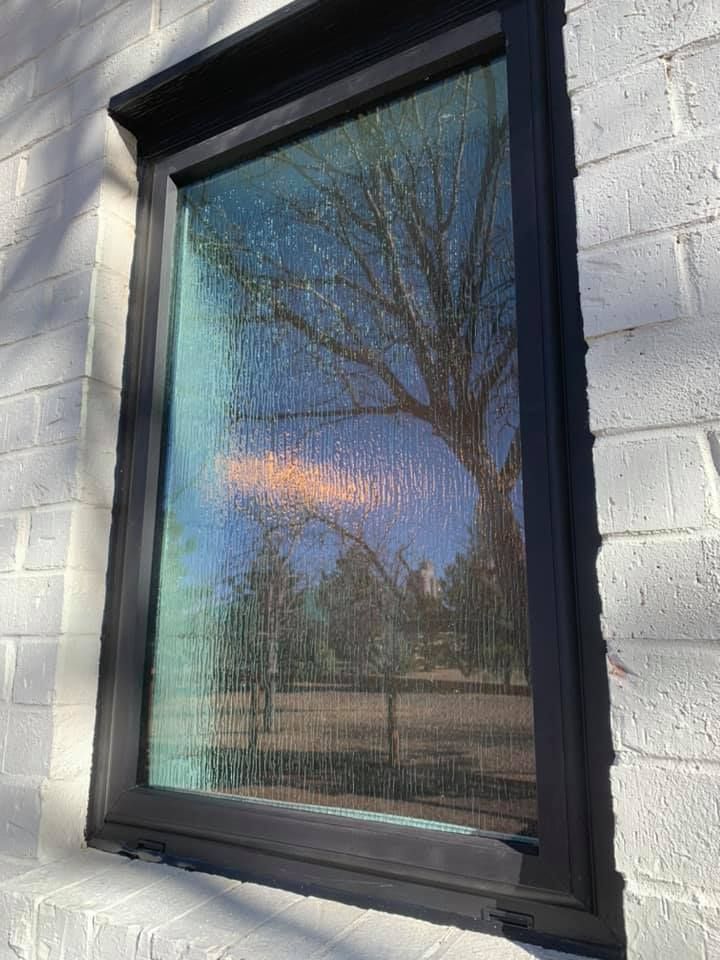 A window with a black frame is on a white brick wall.