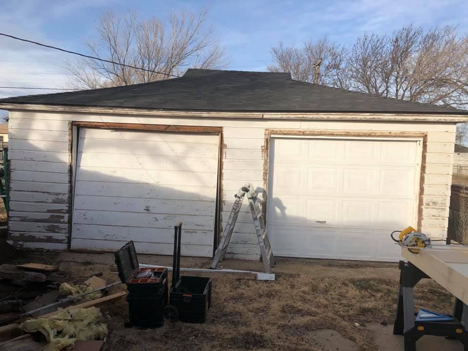 A white garage with a black roof is being remodeled.