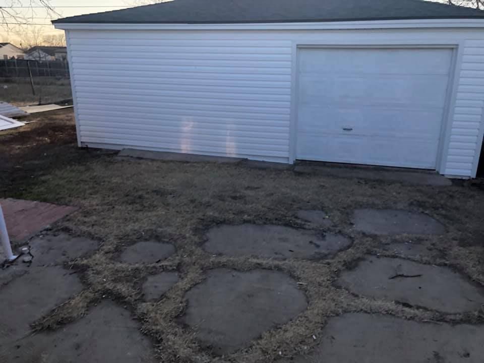 A white garage with a black roof and a concrete driveway in front of it.