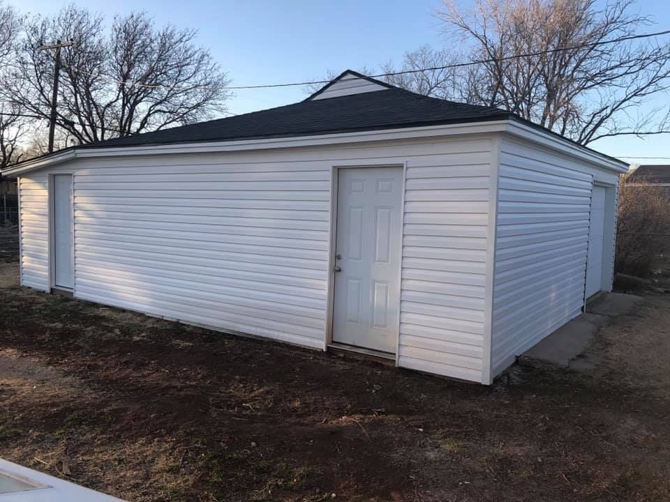 A white garage with a black roof is sitting in the middle of a field.