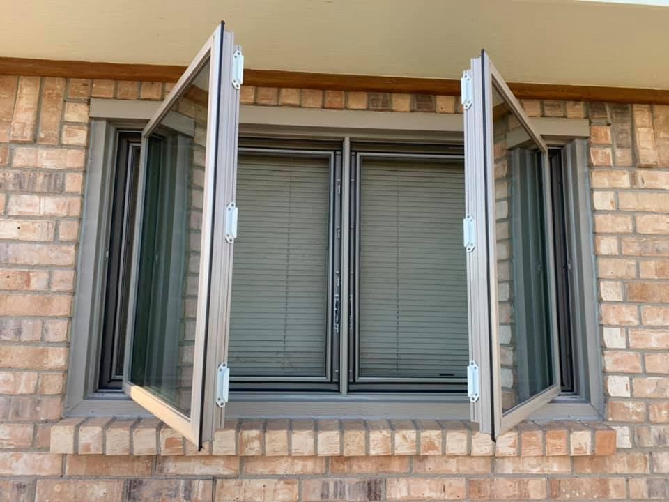 A brick building with two windows open and blinds on them.
