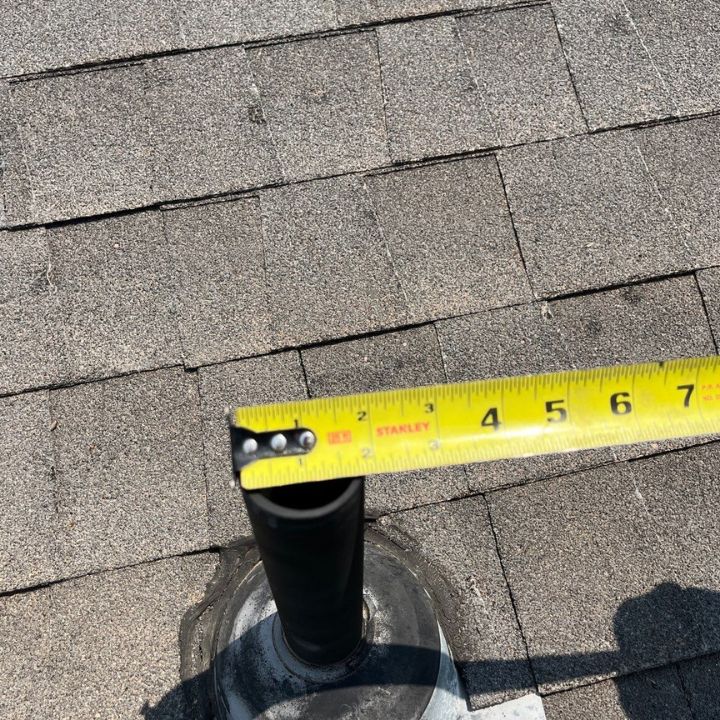 A tape measure is measuring a pipe on a roof.