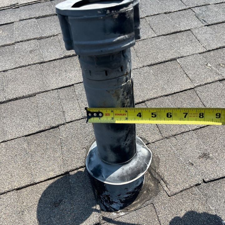 A tape measure is measuring a pipe on a roof.