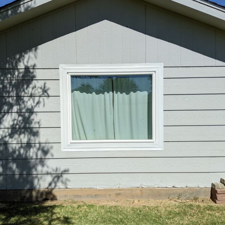 A window on the side of a house with a white frame