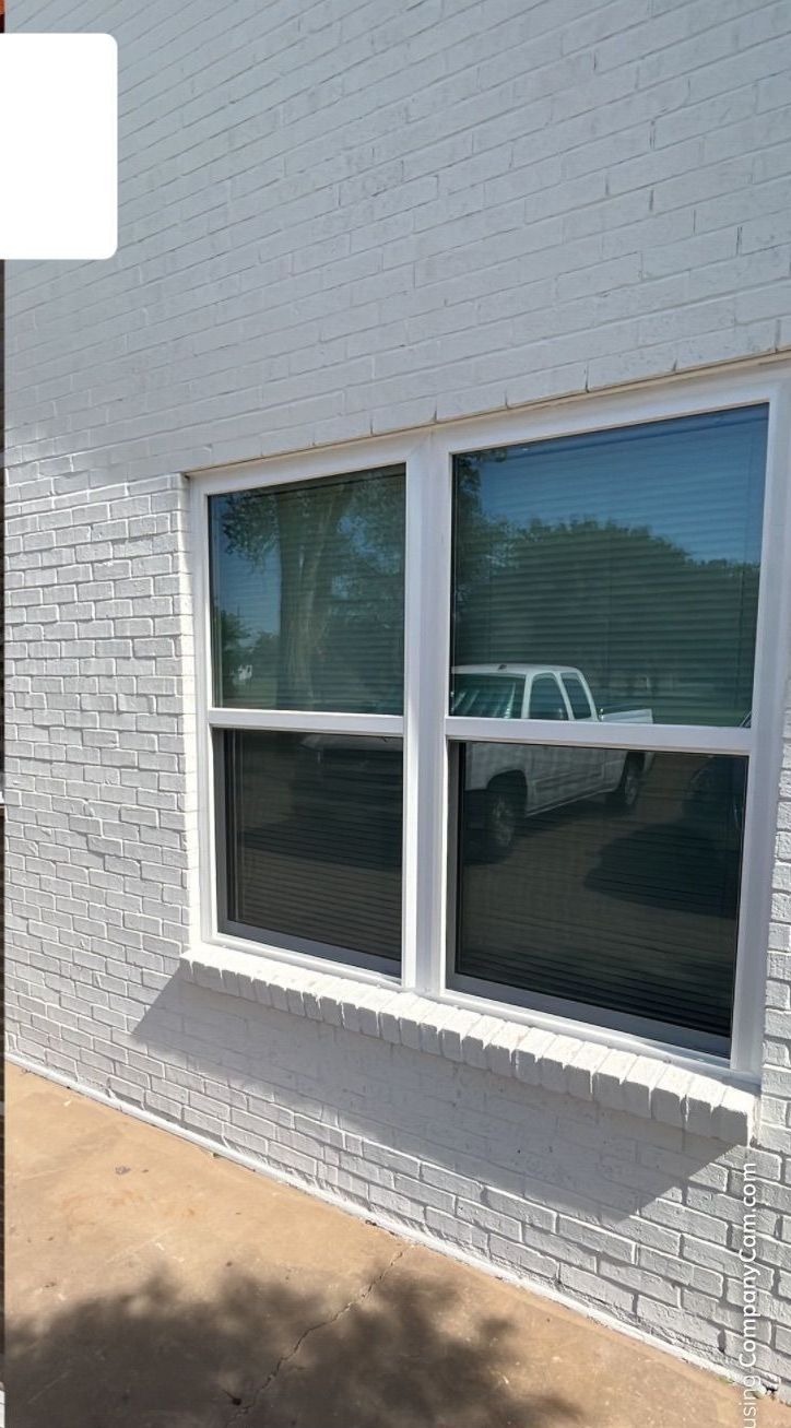 A white brick building with two windows and a white truck parked in front of it.