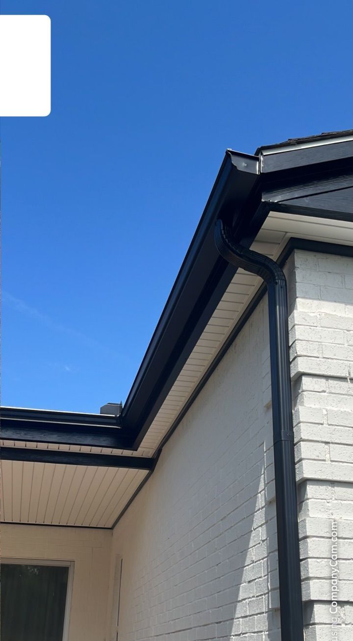 A white brick house with a black gutter and a blue sky in the background.
