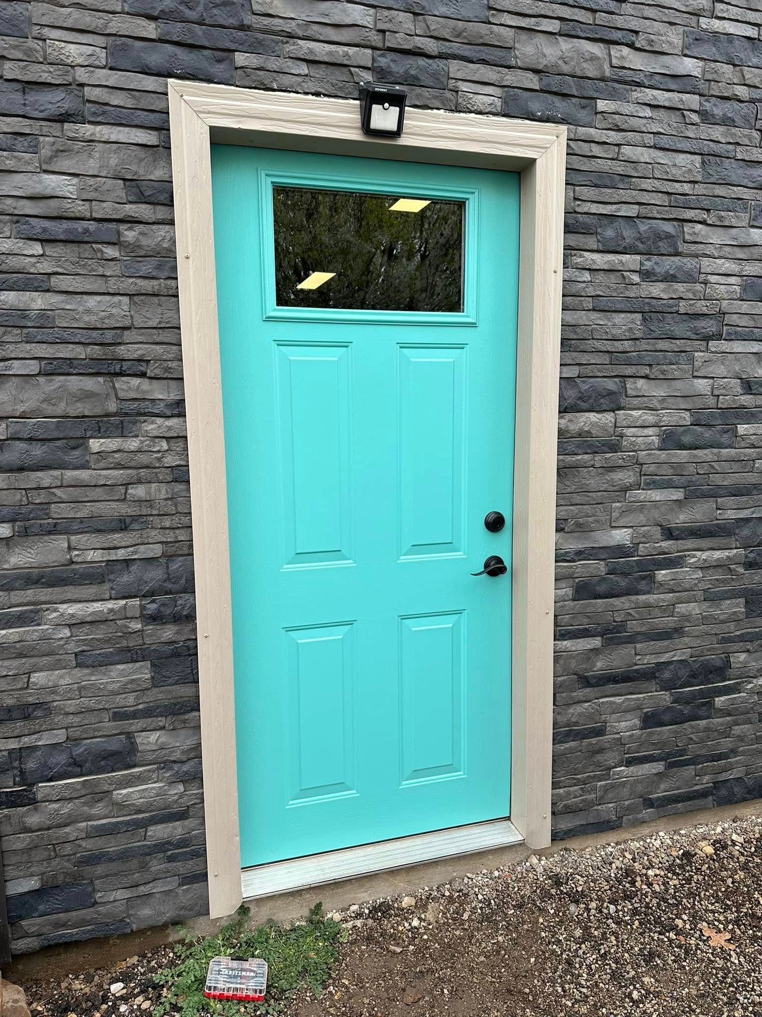 A blue door with a small window is on a brick wall.