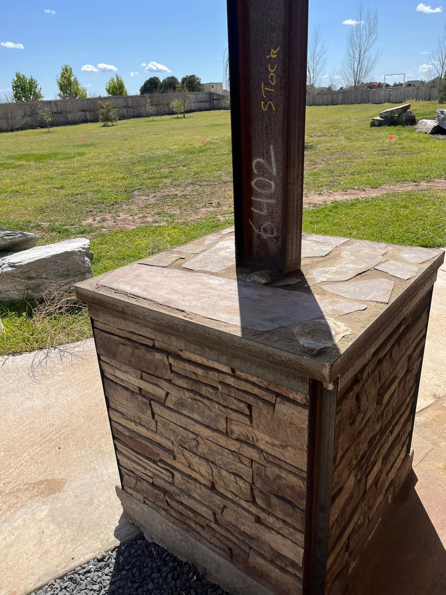 A wooden post is sitting on top of a brick base in a field.