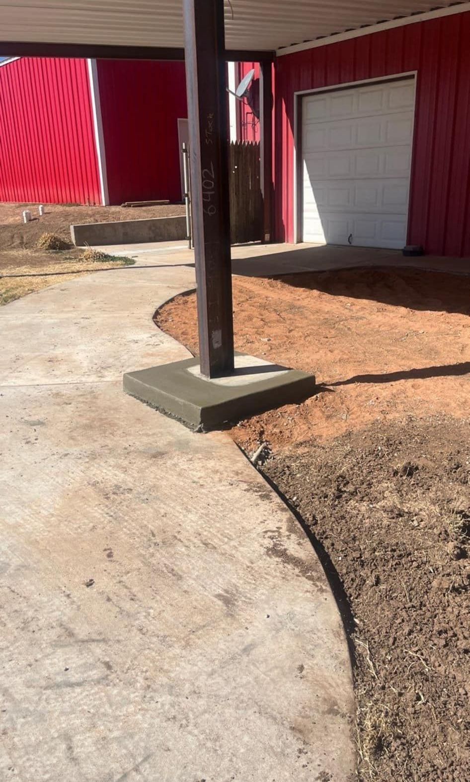 A concrete walkway leading to a garage with a red barn in the background.
