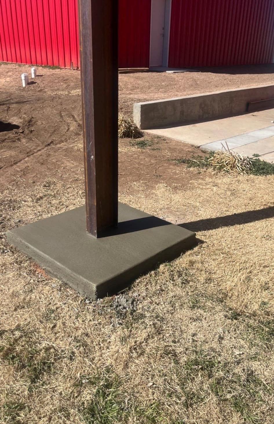 A wooden pole is sitting on top of a concrete base in the grass.