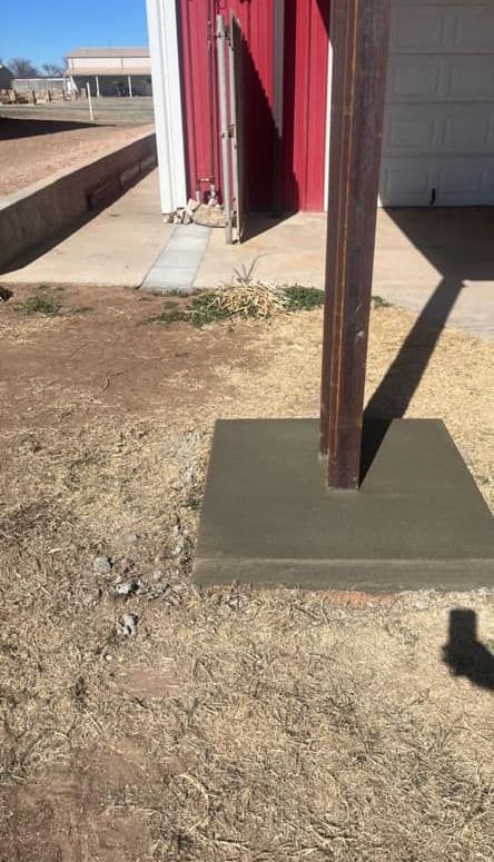 A wooden pole is sitting on top of a concrete base in front of a red barn.