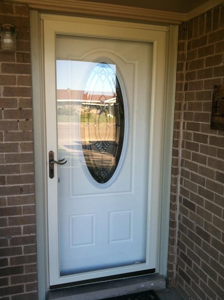 A white door with an oval window is on a brick wall.