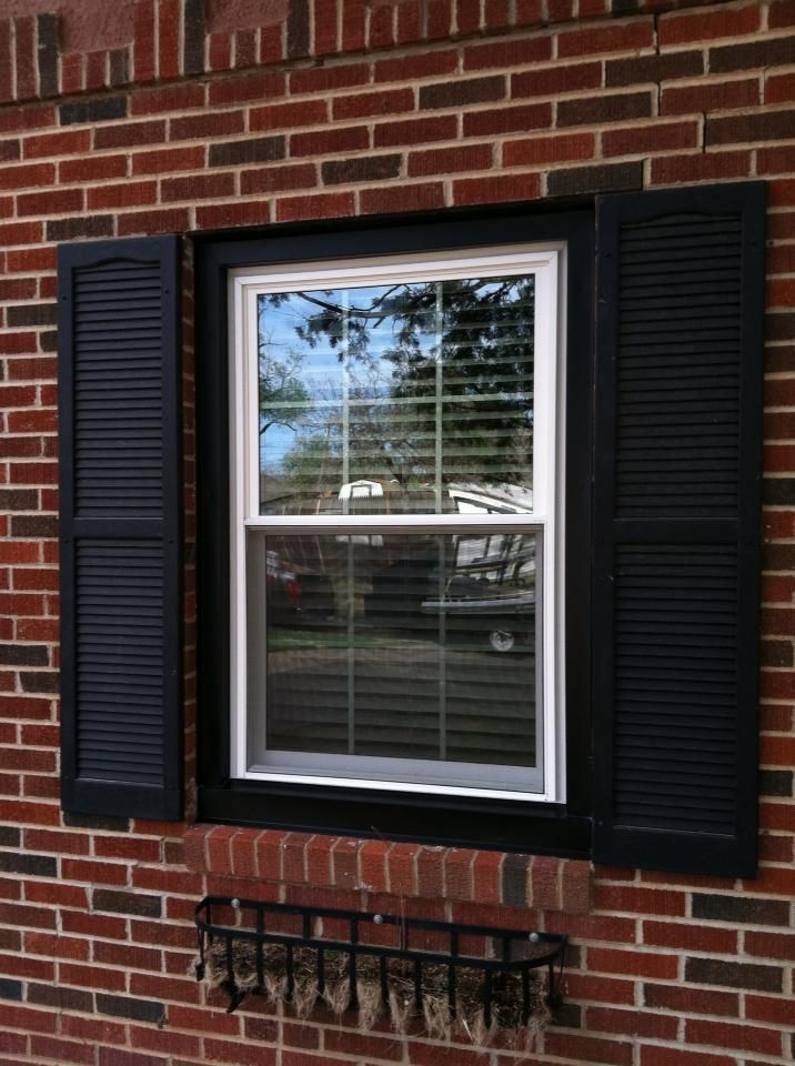 A window with black shutters on a brick wall