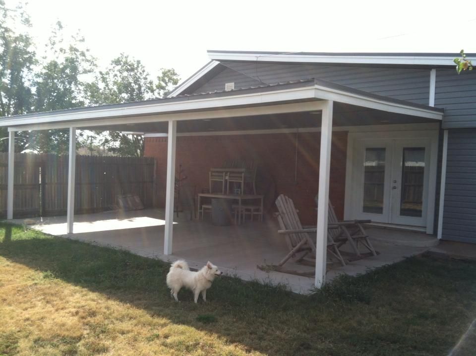 A white dog is standing under a covered patio in front of a house.