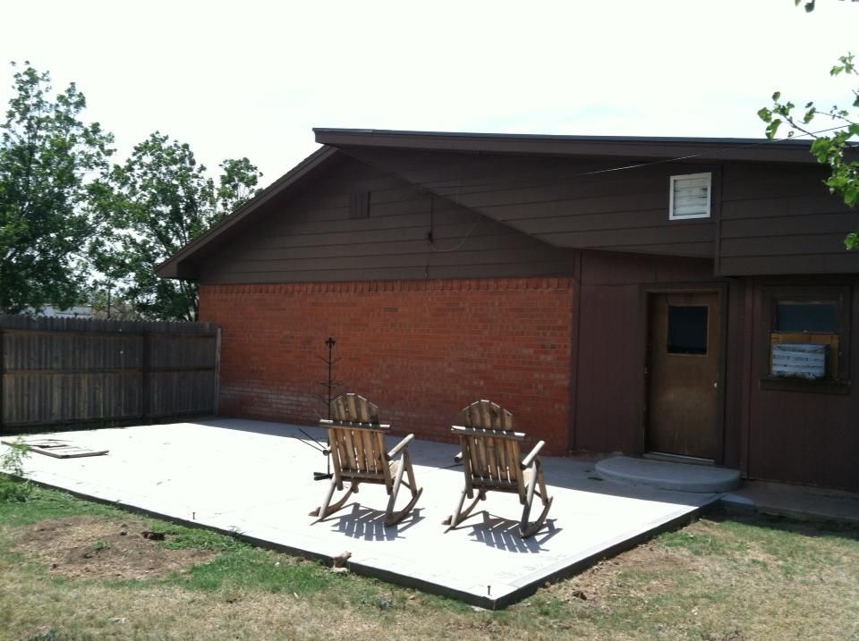 Two rocking chairs are sitting on a concrete patio in front of a house.