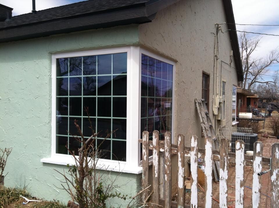 A green house with a white window and a white picket fence