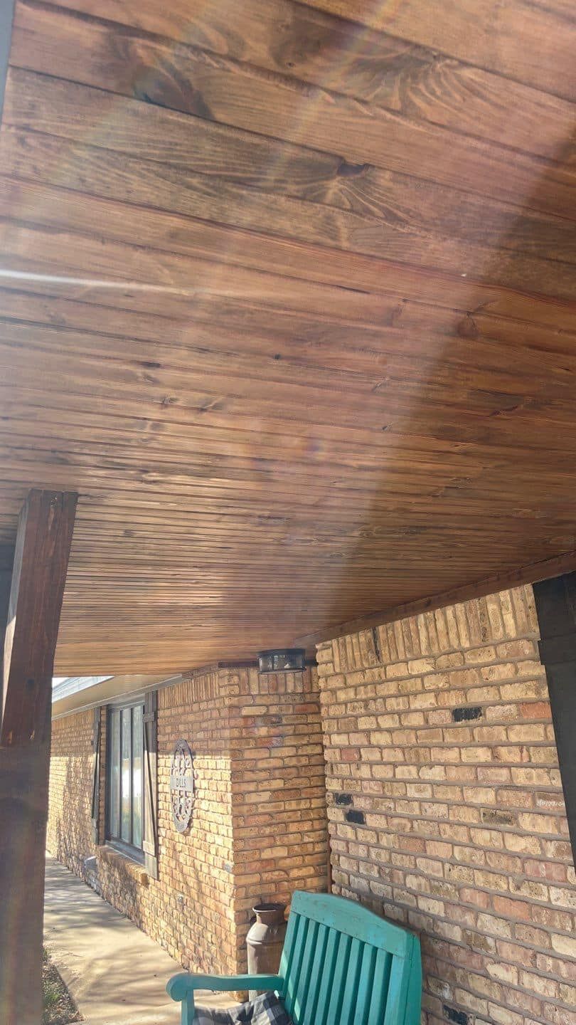 A dog is sitting on a green bench under a wooden porch.