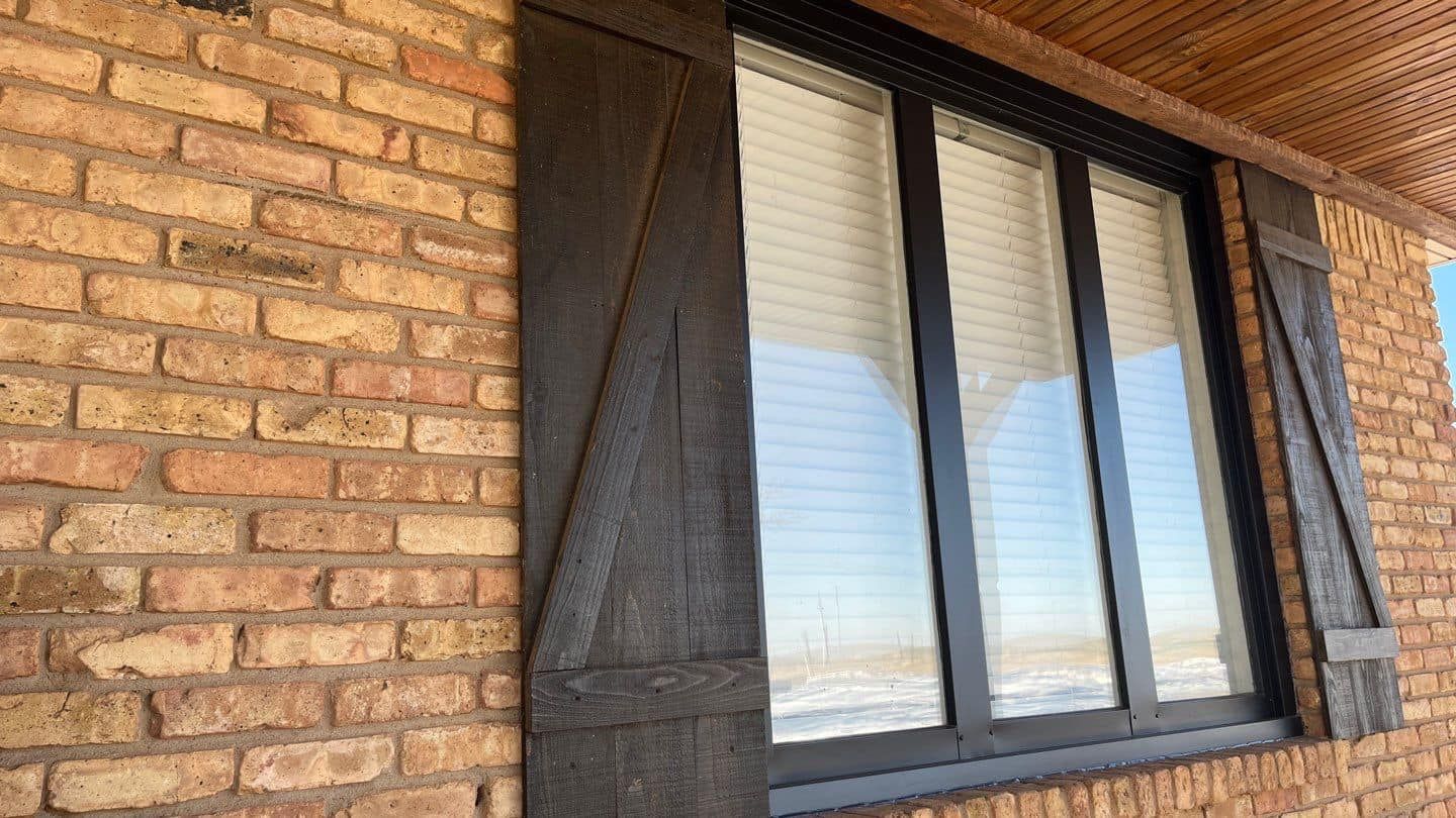 A brick wall with a window and shutters on it.